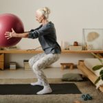 Aged woman doing squats with fitball