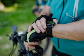 Close-up of senior man biker setting and looking at sports smartwatch, checking his performance.