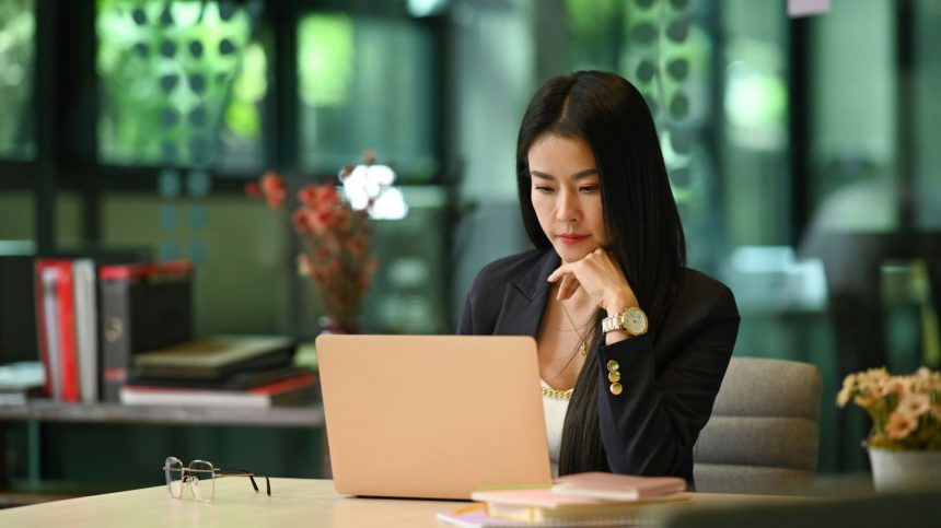 Focused millennial woman entrepreneur reading business information on her laptop computer.