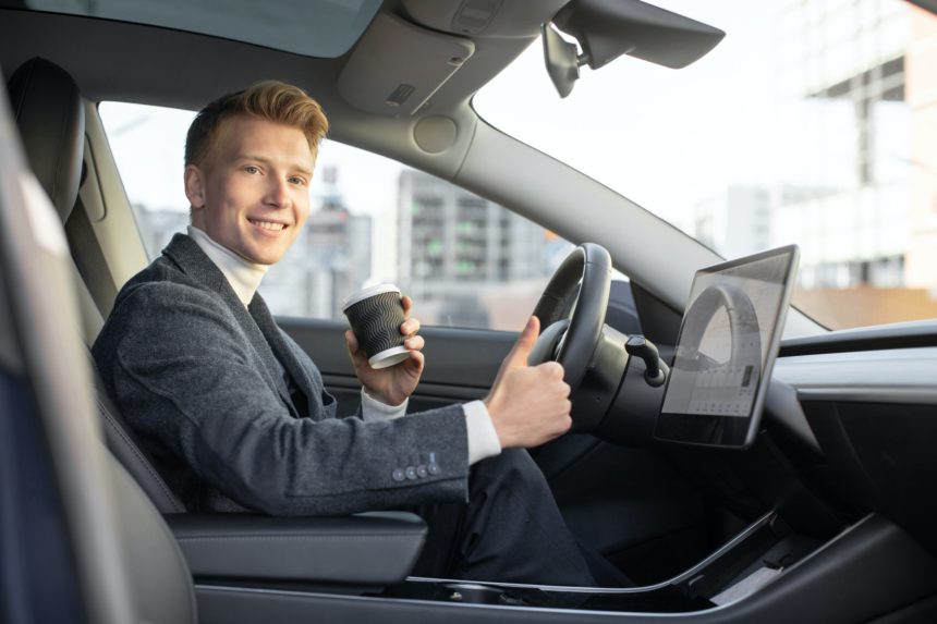 Handsome smiling Caucasian business man riding autonomous car, drinking coffee to go