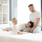 Kid sitting on bed near parents at home in morning