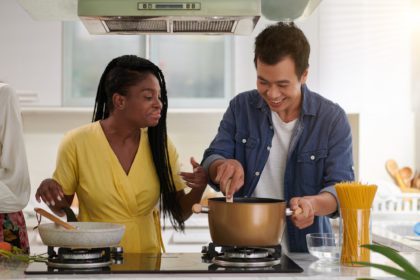Young intercultural couple in casualwear preparing spaghetti